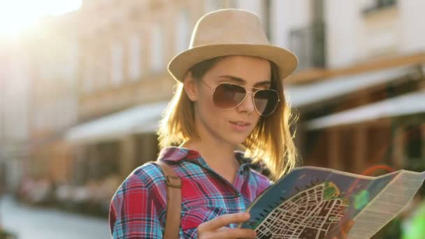태양 안경 일몰 시 아름 다운 오래 된 도시에서 여행 하는 동안 지도 사용 하 여 세련 된 모자에와 아름 다운 젊은 여자의 총 닫습니다. — 비디오