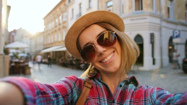 Retrato de mujer joven atractiva en gafas de sol con sombrero posando en la cámara en la calle de la ciudad. Primer plano turista — Vídeo de stock