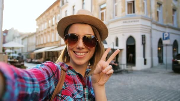 Портрет молодой привлекательной женщины в солнцезащитных очках в шляпе, позирующей на камеру с различными эмоциями на городской улице. Закрыть — стоковое видео