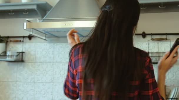 Mujer atractiva con auriculares escuchando música en su smartphone y bailando en la cocina. De cerca. — Vídeo de stock