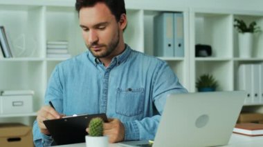 Genç adam rahat giydiriyoruz nihai finansal rapor dizüstü bilgisayarda office arka planda kontrol.