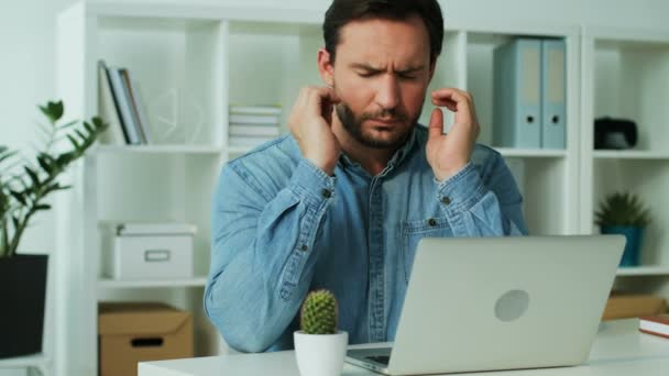Sérieux jeune homme d'affaires en chemise bleue finissant le travail sur l'ordinateur portable dans le bureau, ayant des maux de tête ennuyeux . — Video