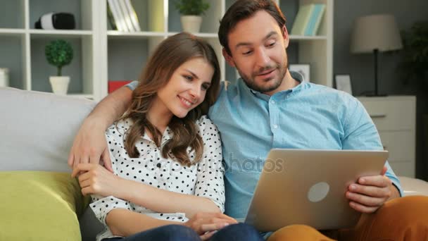 Emocionální atraktivní pár na dovolené na pohovce v obývacím pokoji při sledování filmu na přenosném počítači doma.