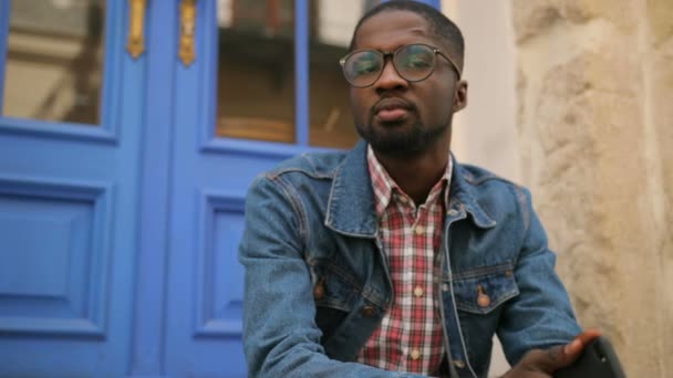 Mladý Američan Afričana muž v brýle vystupuje a usmívá se na kameru na pozadí modré dveře. — Stock video