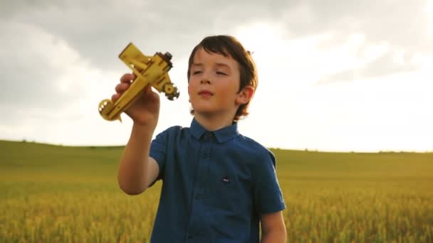 Portret van mooie jongen spelen met houten vliegtuig op de achtergrond van een veld tijdens zonsondergang. — Stockvideo