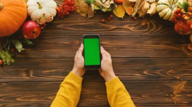 Sonbahar düz kabak ile yatıyordu, akçaağaç ahşap masa üstüne bırakır. Siyah smartphone ile yeşil ekran dikey pozisyonda kadın elle. Üstten Görünüm. Chroma anahtar