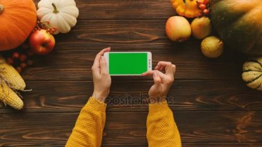 Sonbahar düz kabaklar, meyve ve sebze kahverengi ahşap masa üzerine yatırın. Kaydırma, dokunarak ve beyaz akıllı telefon yatay pozisyonda yeşil ekran ile sayfa yakınlaştırma kadın. Chroma anahtar. Sayfanın Üstü