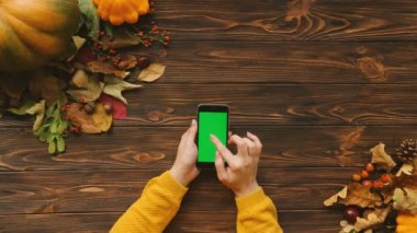 Sonbahar kompozisyon ile akçaağaç yaprakları, kabak ve ahşap masa üstünde siyah smartphone. Üstten Görünüm. Kaydırma, dokunmatik ekranda dokunarak bir kadın. Chroma anahtar
