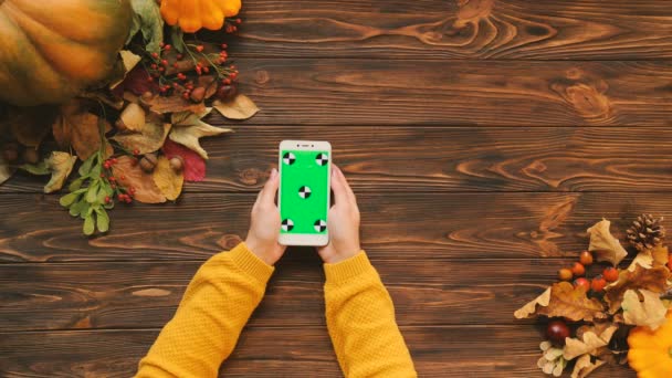 Herfst samenstelling van witte smartphone met groen scherm en esdoorn bladeren en pompoen op bruin houten tafel. Bovenaanzicht. Chromakey. volgen van beweging — Stockvideo