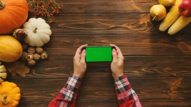 Kaydırma ve siyah smartphone ile yatay pozisyonda yeşil ekran sayfalarında swiping kadın. Tablo yukarıdan Sonbahar meyve ve sebze ile. Chroma anahtar.