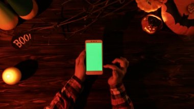 Üstten Görünüm. Helloween tatil tasarım. Balkabağı, koyu ahşap masa mum. Yeşil perde ile akıllı telefon kullanan kadın. Chroma anahtar