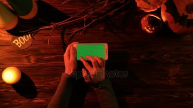 Ahşap masa üzerinde Halloween üstten görünüm pumpkins, mumlar, yarasalar ve yeşil ekran ile beyaz smartphone ile. Kaydırma, dokunmatik ekranda dokunarak bir kadın. Chroma anahtar