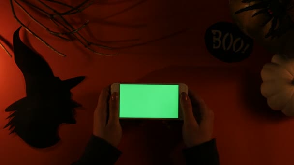 Vista dall'alto. Concetto Helloween. Woamn utilizzando msartphone con schermo verde su tavolo arancione con decorazione vacanza. Piatto. Chiave cromatica — Video Stock