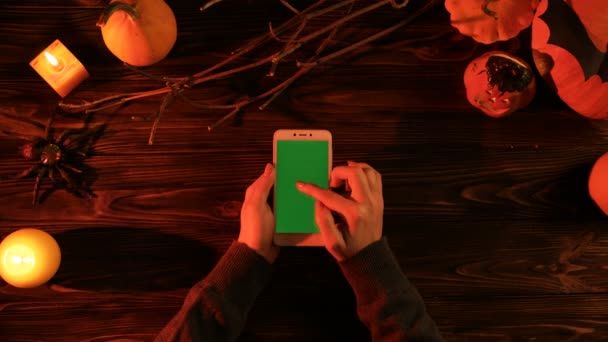 Vista superior da decoração do halloween na mesa de madeira. Mulher tocando no smartphone com tela verde no escuro. Chave Chroma. Depósito plano — Vídeo de Stock