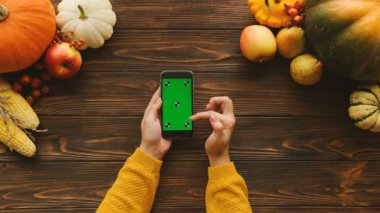 Tablo yukarıdan Sonbahar temalı. Siyah smartphone yeşil ekran ve üzerinde ahşap masa etrafında sebze ve meyve ile. Kaydırma, dokunmatik ekranda dokunarak parmaklar. Chroma anahtar. İzleme