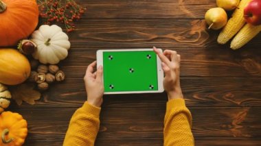Ahşap masa üzerinde yatay konumda yeşil ekran ile beyaz tablet aygıtı kullanan kadın. Masada sonbahar üstten görünüm meyve ve sebze ile. Chroma anahtar. Hareket izleme