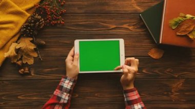 Tablo üstten görünüm kitaplar, kazak, akçaağaç ahşap masanın üzerine bırakır. Kaydırma, beyaz tablet cihaza yeşil ekran ile dokunarak bir kadın. Yatay konum. Chroma anahtar