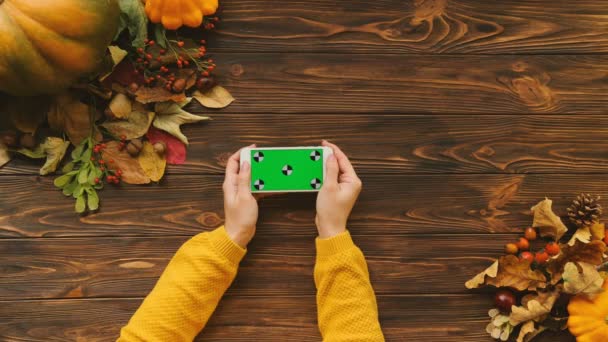 Φθινοπωρινή σύνθεση του maple φύλλα, κολοκύθες και λευκό smartphone με πράσινη οθόνη σε οριζόντια θέση πάνω στο ξύλινο τραπέζι. Κλειδί Chroma. Το Top view. Παρακολούθηση κίνησης. Επίπεδη θέσει — Αρχείο Βίντεο