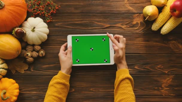 Woman using white tablet device with green screen in horizontal position on the wooden table. Autumn top view with fruits and vegetables on the table. Chroma key. Tracking motion — Stock Video