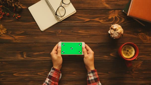 Witte smartphone met groen scherm, notebook, bril, tea cup op de houten tafel. Bovenaanzicht. Chromakey. Volgen van beweging — Stockvideo