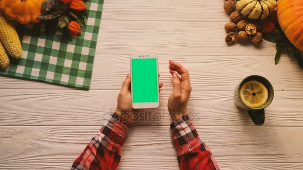 Bovenaanzicht van fruit, groenten, noten op de witte houten tafel. Vrouw met behulp van smartphone met groen scherm. Flat lag. Chromakey — Stockvideo