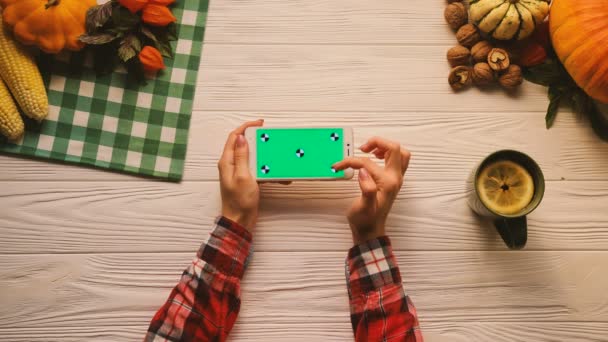 Autumn top view flat lay with fruits, nuts and vegetables on the white wooden table. Woman scrolling, tapping, zooming pages on smart phone with green screen. Horizontal position. Tracking motion — Stock Video