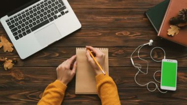 Gelecek yıl 2018 planlar sarı kazaklı kadın. Kadın not defterinde ahşap masanın üzerine yazma. Beyaz snartphone yeşil ekran ile. Chroma anahtar. Üstten Görünüm