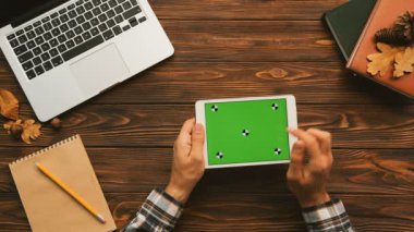 Adam beyaz tablet cihaza yeşil ekran ile dokunarak. Yatay. Hareket izleme. Ahşap masa artalanını dizüstü bilgisayar ve dizüstü bilgisayarlar. Üstten Görünüm