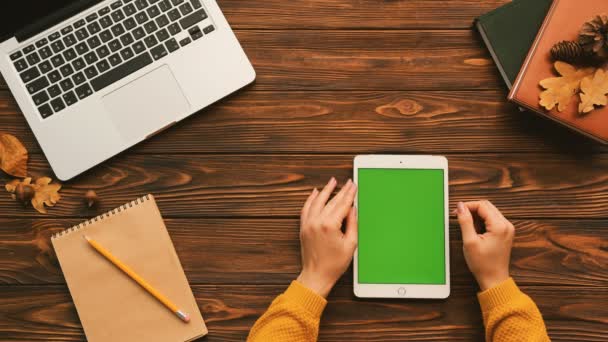 Top view of woman tapping, swiping, zooming on the white tablet device with green screen on the woosen table with laptop and notebooks. Учеба, серфинг интернет. Хрома-ключ. Вертикаль — стоковое видео