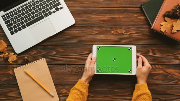 Frau tippt auf das weiße Tablet-Gerät mit grünem Bildschirm. horizontal. Tracking-Bewegung. Holztischhintergrund. Ansicht von oben — Stockvideo