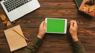 Tablet bilgisayar üzerinde ahşap masa kullanan adam. Üstten Görünüm vurdu. Erkek parmak kaydırma, yeşil ekrana dokunarak. Chroma anahtar.