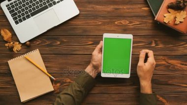 Dizüstü bilgisayar ve dizüstü bilgisayarlar ile ahşap tabloda tablet bilgisayar kullanan adam. Üstten Görünüm vurdu. Erkek parmak kaydırma, yeşil ekrana dokunarak. Chroma anahtar. Dikey