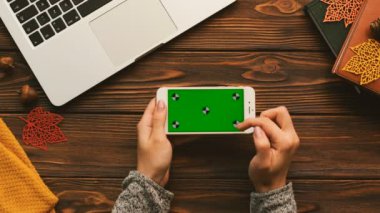 Üstten Görünüm kaydırma, dizüstü bilgisayar, kitap ile ahşap masa üstünde yeşil perde ile belgili tanımlık smartphone dokunmatik ekranda dokunarak wooman. Hareket izleme. Yatay