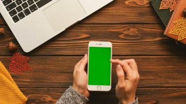 Ahşap masa üstünde yeşil perde smartphone kullanarak wooman sıcak üstten görünüm. Kaydırma, dokunarak, sayfa yakınlaştırma parmak. Chroma anahtar.