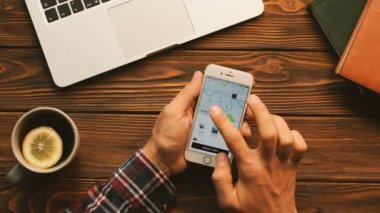 New York - 10 Eylül 2017: Uber app üzerinde beyaz smartphone kullanan adam. Sipariş bir araba, taksi, taksi adam. Ahşap masa arka plan üzerinde atış Üstten Görünüm.