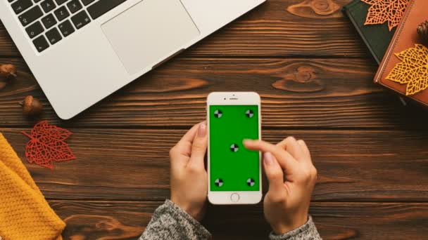 Kvinna rullning, knacka på pekskärmen på din smartphone med grön skärm på trä bordet med laptop, böcker. Spåra rörelse. Ovanifrån — Stockvideo