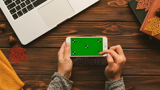 Bovenaanzicht van wooman scrollen, te tikken op het touchscreen van de smartphone met groen scherm op de houten tafel met laptop, boeken. Het bijhouden van beweging. Horizontale — Stockvideo