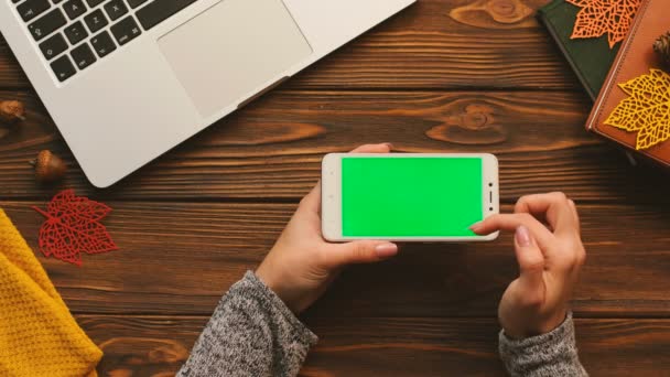 Herbst-Draufsicht. Frau tippt, zoomt grüne Bildschirmseiten auf dem Smartphone. Holzschreibtisch Hintergrund. Chroma-Schlüssel. horizontal. — Stockvideo