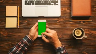 Ahşap masa arka planında dizüstü bilgisayar, dizüstü bilgisayar ve çay yeşil ekran ile smartphone üzerinde çalışan adam. Üstten Görünüm. Chroma anahtar