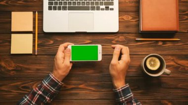 Üstten Görünüm dokunarak, yakınlaştırma, beyaz smartphone ile ahşap masa üzerinde yatay konumda yeşil ekran sayfalarında kaydırma adamın. Üstten Görünüm. Okuyan adam. Chroma anahtar