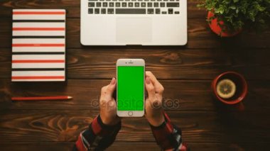Tablo üstten görünüm kırmızı öğeler ile. Kadın swiping, yakınlaştırma sayfalarla kahverengi ahşap masa üstünde yeşil perde smartphone. Chroma anahtar