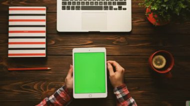 Kırmızı öğeler ile renkli tablo üstten görünüm. Kadın swiping, kahverengi ahşap masa üstünde yeşil perde ile tablet bilgisayar üzerindeki yakınlaştırma sayfaları. Chroma anahtar