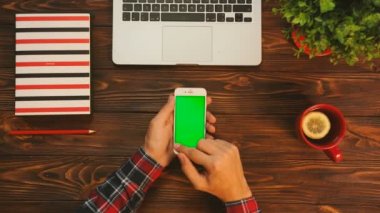 Dostum swiping, dokunarak, smartphone aygıt sayfalarında yeşil ekran kaydırma. Ahşap masa arka plan. Üstten Görünüm. Chroma anahtar