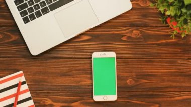 Üstten Görünüm ile kırmızı öğeler ve dizüstü bilgisayar ile ahşap tabloda dikey pozisyonda Yeşil perde beyaz akıllı telefon. Chroma anahtar