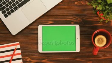 Ahşap masa üstünde yeşil perde beyaz tablet bilgisayar. Chroma anahtar. Üstten Görünüm. Kırmızı çay Kupası, dizüstü bilgisayar ve dizüstü bilgisayar