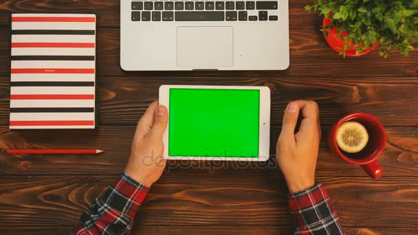 Flat lay com caneca de chá vermelho, notebook colorido, computador portátil e tablet branco dispositivo com tela verde na mesa de madeira. Um homem a tocar no ecrã táctil. Posição horizontal. Chave Chroma — Vídeo de Stock