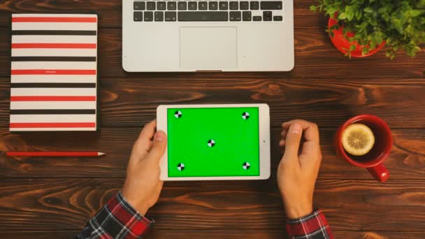 Hombre trabajando en la tableta blanca con pantalla verde. Movimiento de rastreo. Clave de croma. Vista superior de la mesa con elementos rojos — Vídeo de stock