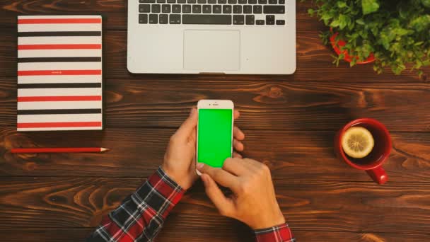 Hombre deslizando, tocando, desplazando páginas de pantalla verde en el dispositivo de teléfono inteligente. Fondo de tabla de madera. Vista superior. Clave de croma — Vídeo de stock