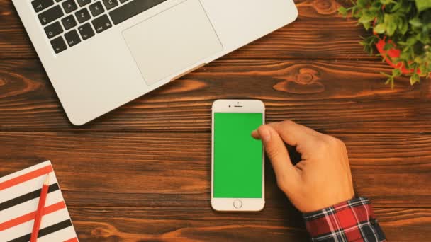 Primer plano dedo masculino tocando en la pantalla verde del teléfono inteligente. Fondo de tabla de madera. Vista superior. Clave de croma — Vídeos de Stock