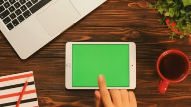 Erkek parmak dokunmatik ekran beyaz tablet cihazın sayfalarında kahverengi ahşap masa üstünde yeşil perde ile kaydırma. Üstten Görünüm. Chroma anahtar. Düz yatıyordu